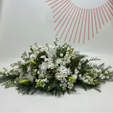 Casket Spray of white and green flowers on a white surface with a pink abstract design in the background